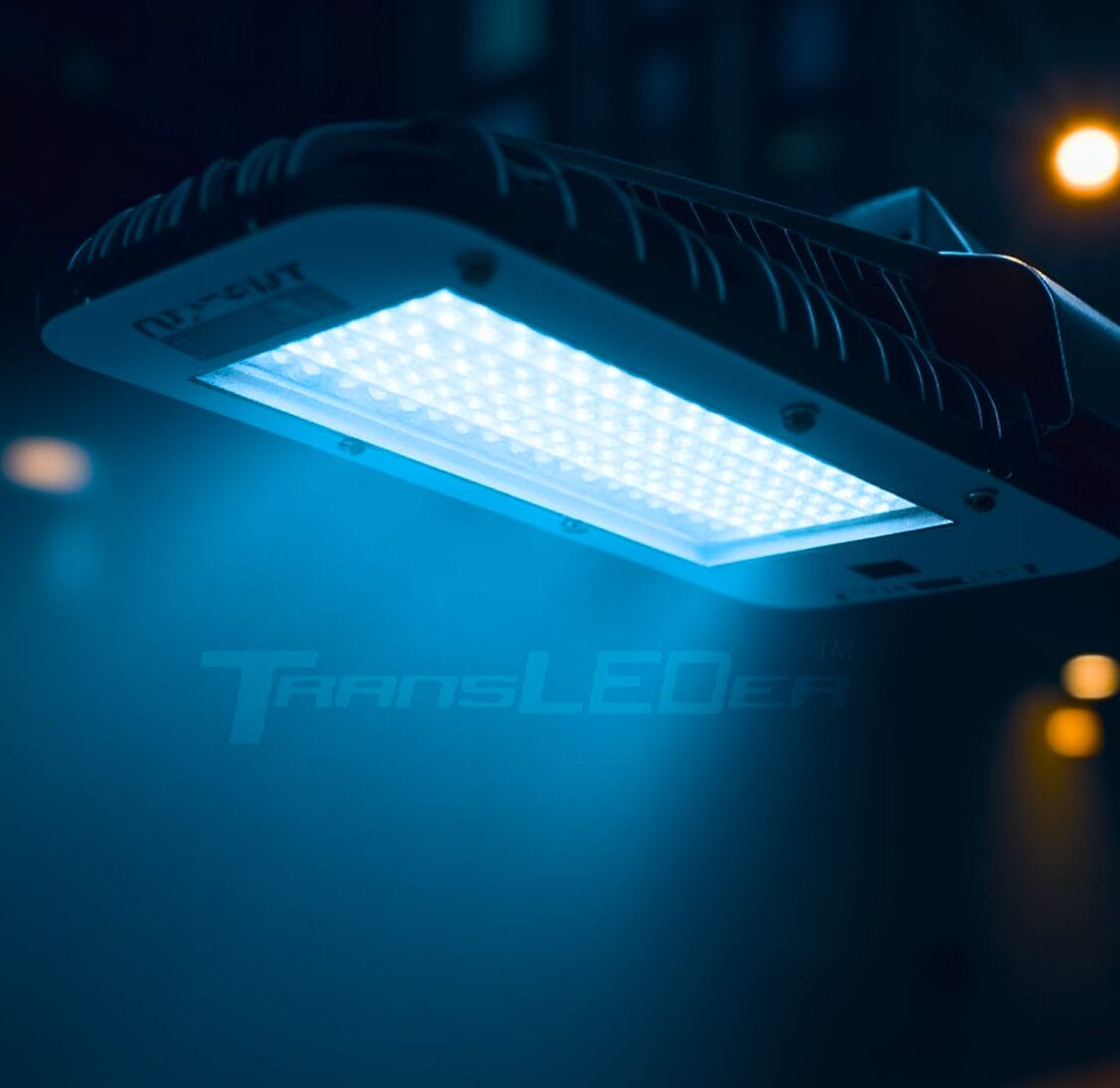 A close-up of an illuminated LED street light with a blue glow, showing the “TransLEDer” brand logo in the background.