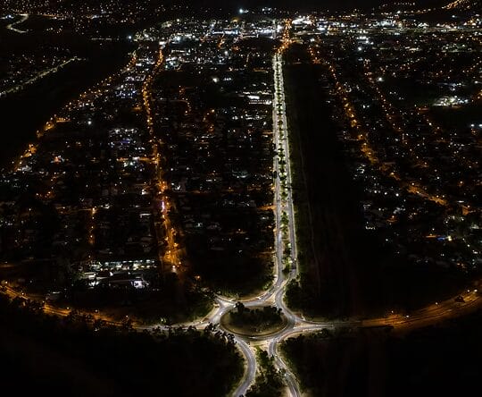 Aerial view of a city at night showing illuminated streets, a roundabout, and buildings with scattered lights.