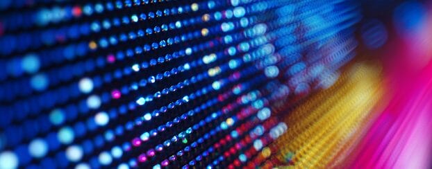 Close-up of a digital LED screen displaying rows of colorful, illuminated pixels in blue, yellow, and pink hues, with a blurred effect.