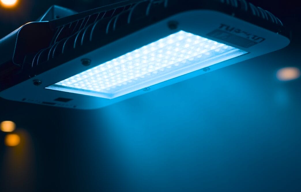 Close-up of an LED panel light emitting a bright blue glow, with a blurred dark background and a few unfocused lights.