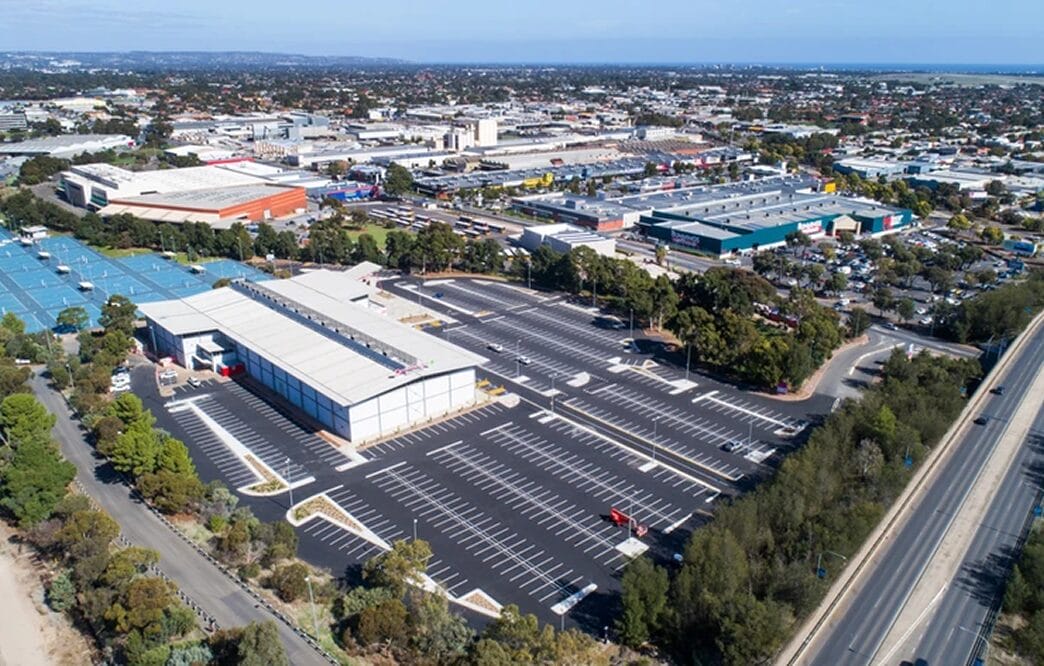 Aerial view of a large commercial complex with multiple warehouses, expansive parking lots, roads, and surrounding urban area.